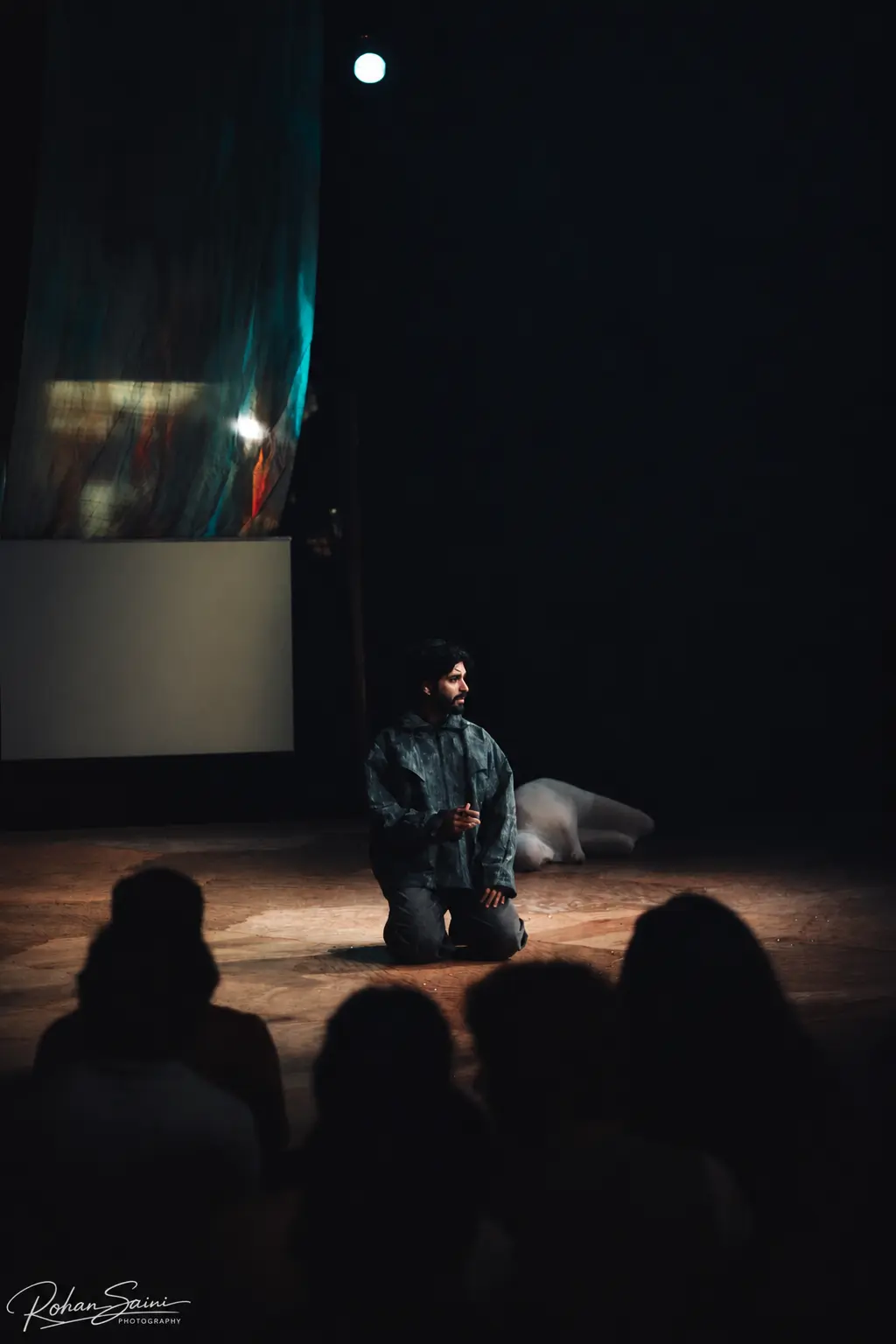 Harshit Dixit kneeling alone in a pool of stage light during PRESÉNT